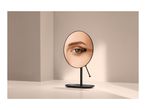A close-up of an eye applying eyeshadow, reflected in a round vanity mirror.
