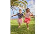 Two girls in Lupilu Kids' T-shirts and skirts playing on grass with palm trees.