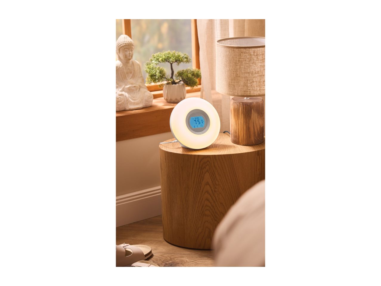 A round wake-up light with a digital display on a wooden bedside table.