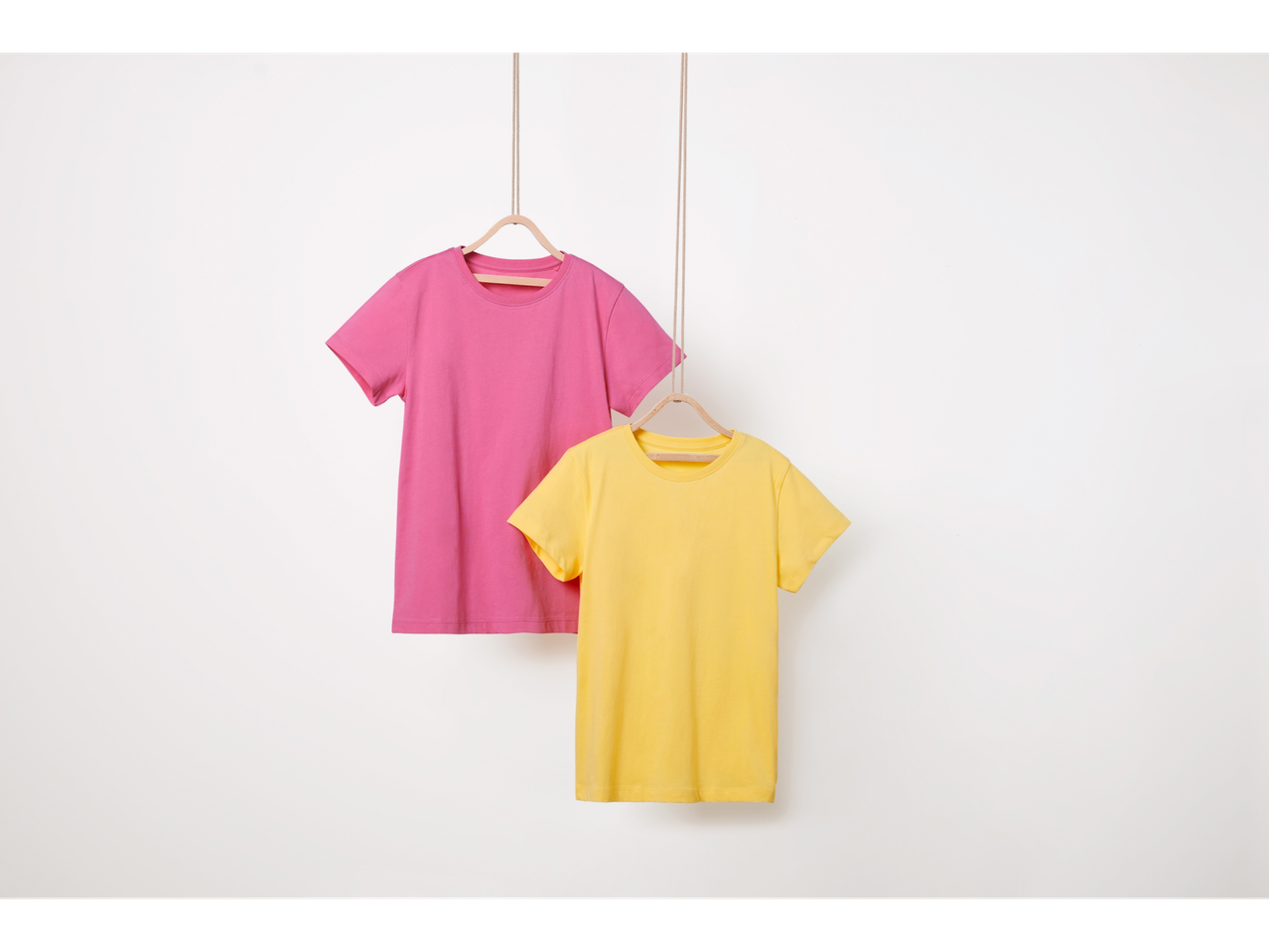 Δύο μονόχρωμα t-shirt, ένα ροζ και ένα κίτρινο, κρέμονται σε κρεμάστρες.