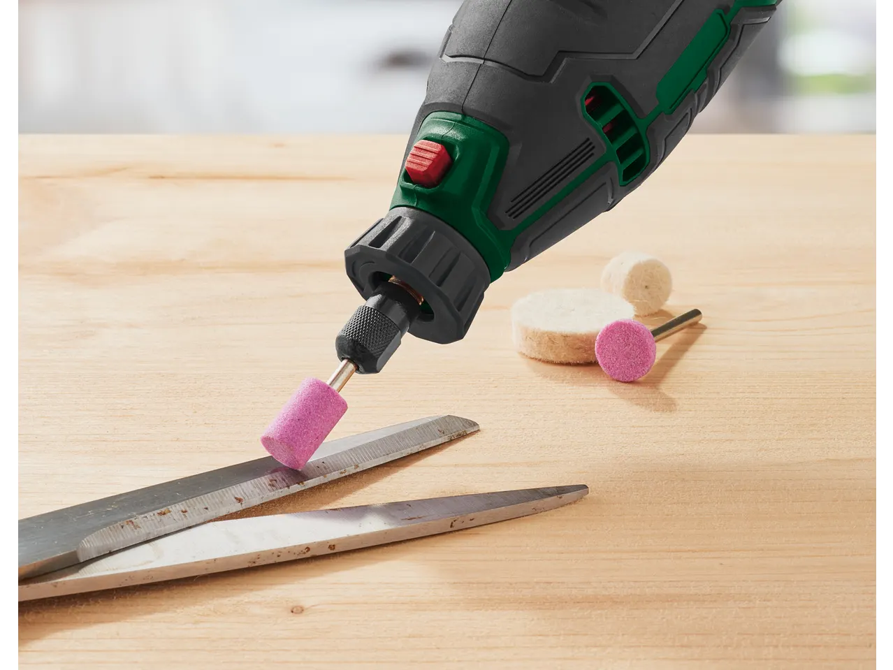 Rotary tool with a pink grinding stone sharpening scissors on a wooden surface.