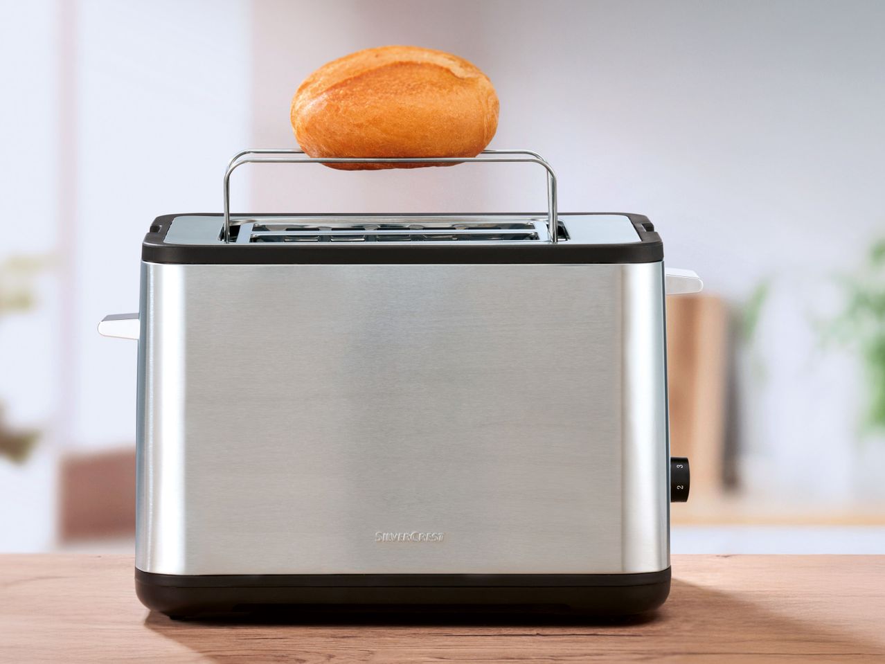 Тостер SilverCrest с поставка за притопляне на хлебче върху дървена маса.