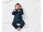 Lachende baby in een Lupilu® merino wollen romper op een witte deken.