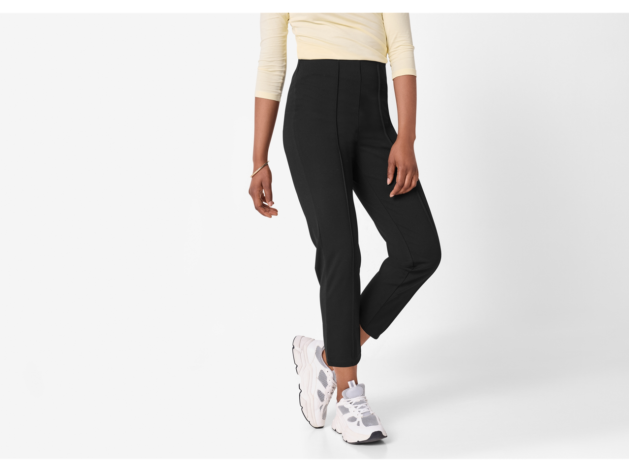 Woman in a light yellow long-sleeve top, black trousers, and white sneakers.