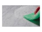 Hand scrubbing a marble surface with a green sponge and cleaning foam.