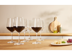 Copo de vinho tinto e sortido de copos vazios com queijo e uvas numa cozinha.