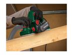 Person using an electric planer on a wooden beam, with a dust extraction hose attached.
