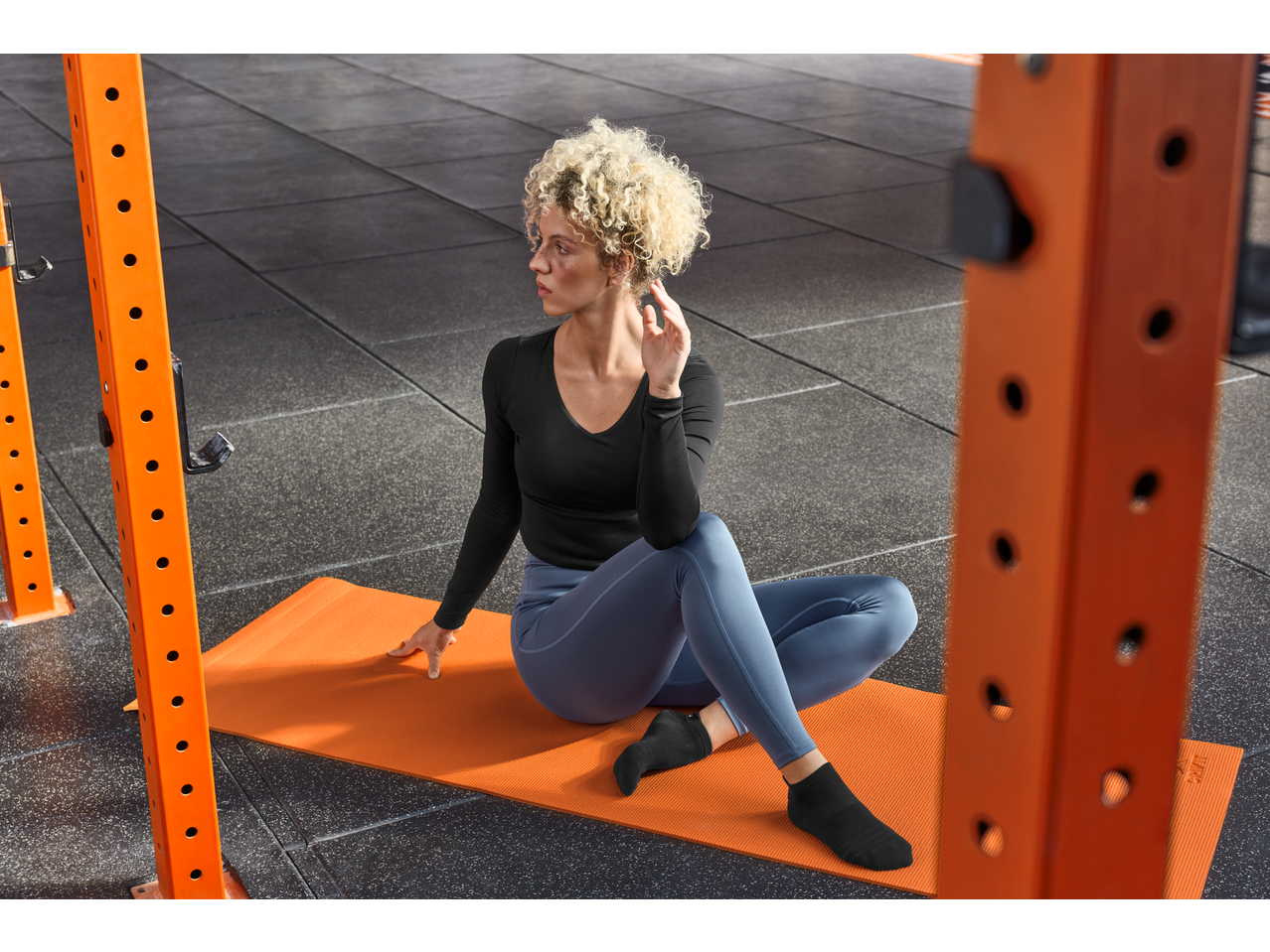 Woman in black long-sleeve top and blue leggings sitting on an orange yoga mat.