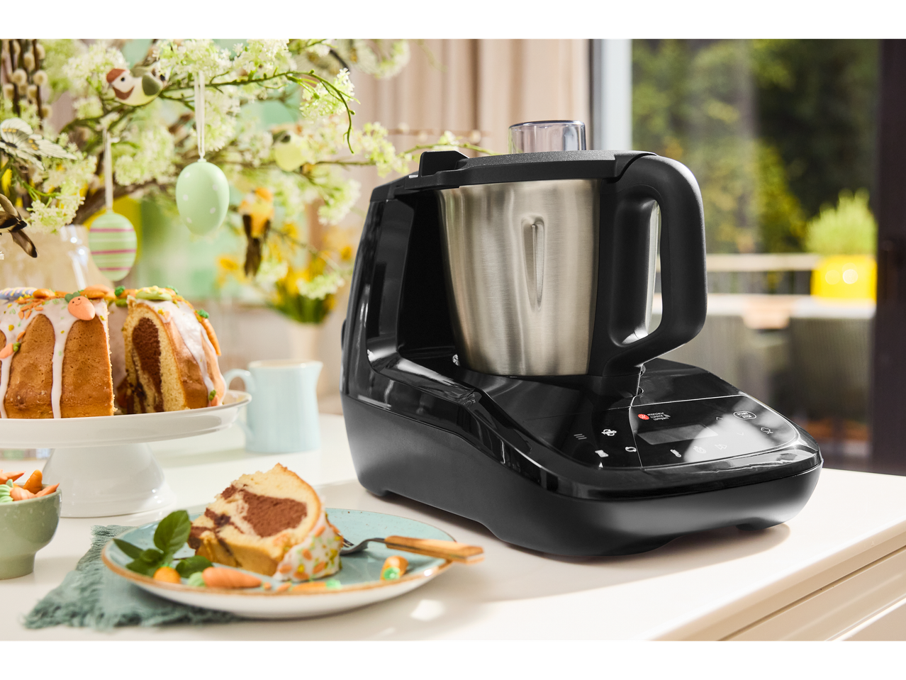 Máquina de cozinha preta com taça, bolo de Páscoa e decorações de Páscoa numa mesa.