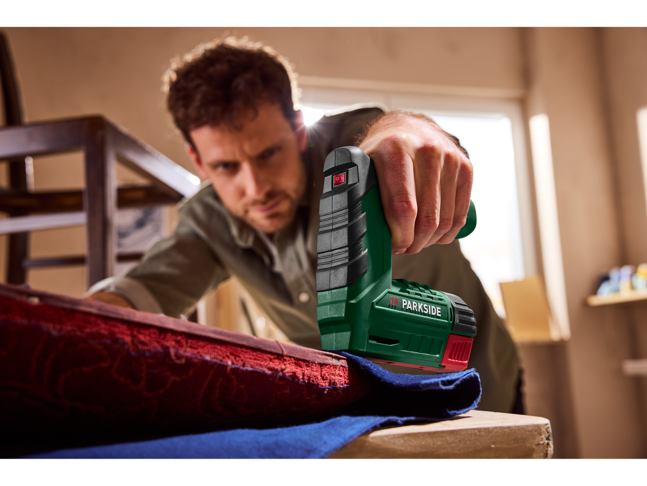 Un bărbat tapițează o piesă de mobilier cu un capsator electric.