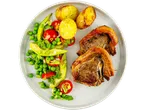 A plate of roasted lamb chops, roasted potatoes, and a fresh pea and avocado salad.