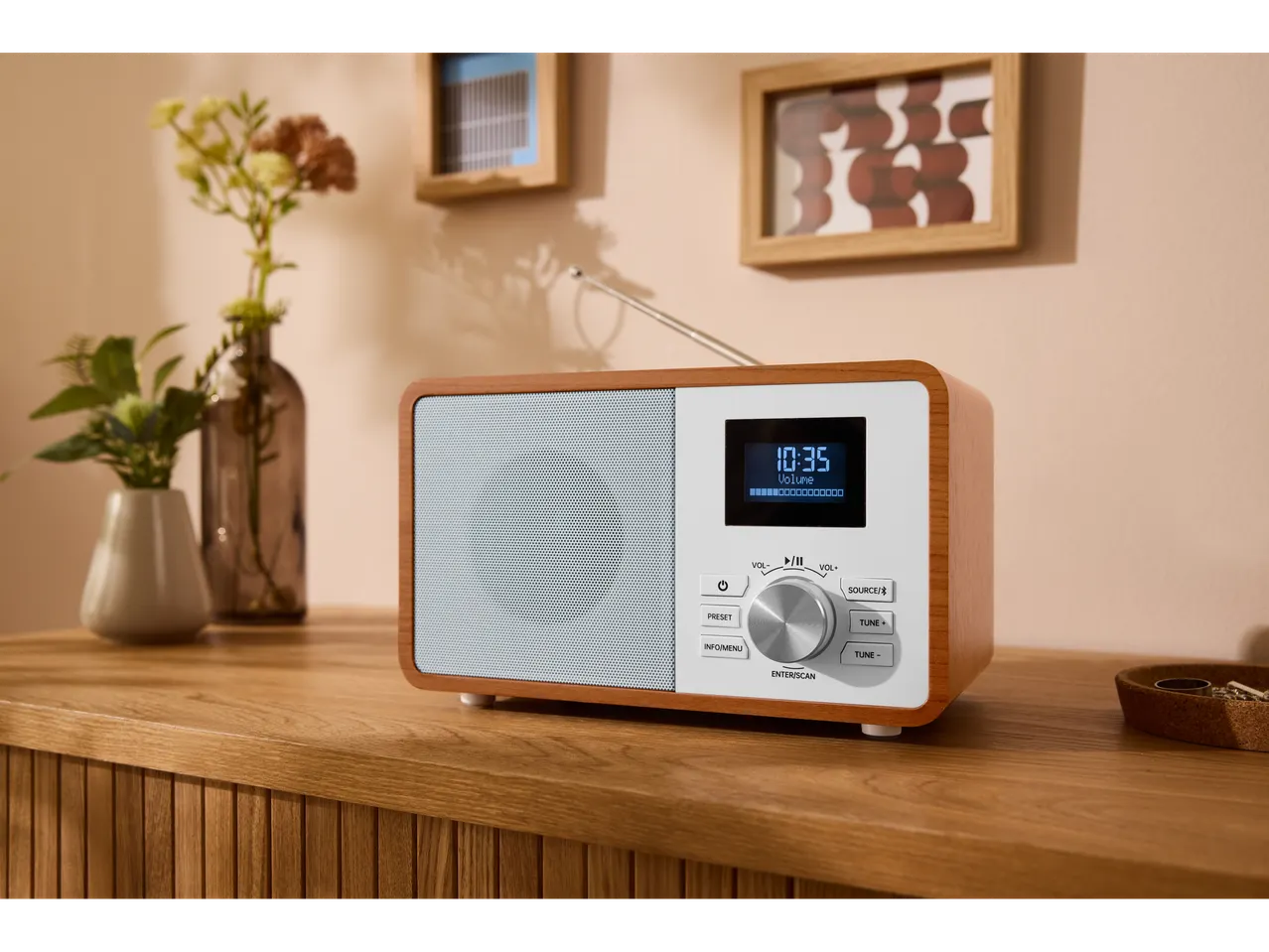 TRONIC® radio na drvenoj komodi, sa vazama i slikama u pozadini.