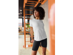 Mulher de t-shirt desportiva branca e calções pretos a alongar-se em ambiente interior.