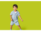 Smiling boy in a light blue short-sleeved shirt and matching shorts on a green background.