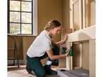 A woman uses a cordless drill to assemble a wooden structure.