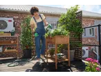 Woman in Parkside® Gardening Gloves watering plants on a rooftop garden.