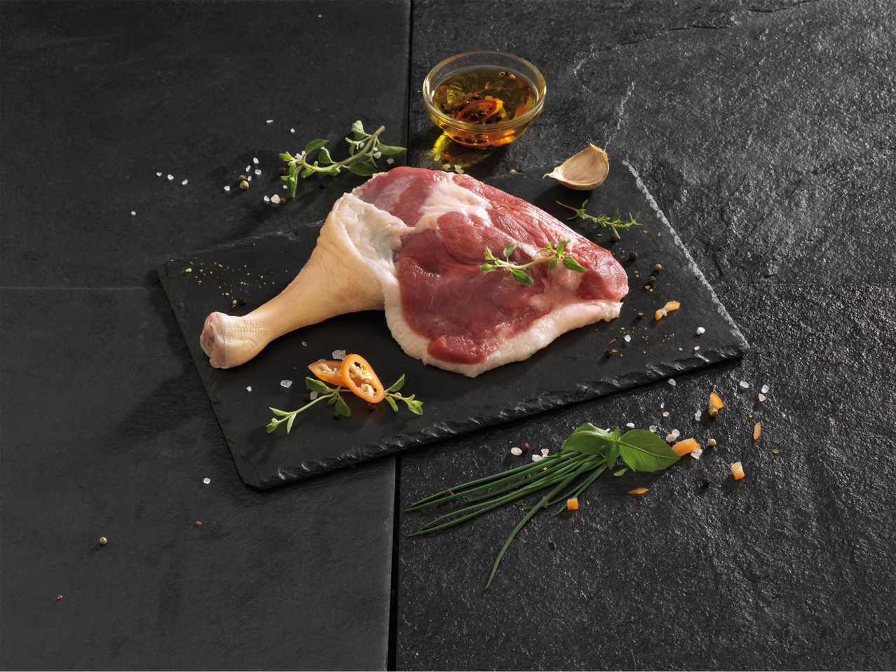 Nyers kacsacomb fűszerekkel és olajjal sötét pala alapon.