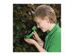 A boy in a green shirt uses a green and black magnifying glass to examine a leaf.