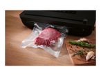 A vacuum sealer packaging a piece of raw meat on a wooden table next to fresh herbs.