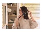 Woman in a bathrobe styling her hair with a hot air brush in a bathroom.
