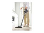 Person vacuuming a rug in a laundry room with a stick vacuum cleaner.