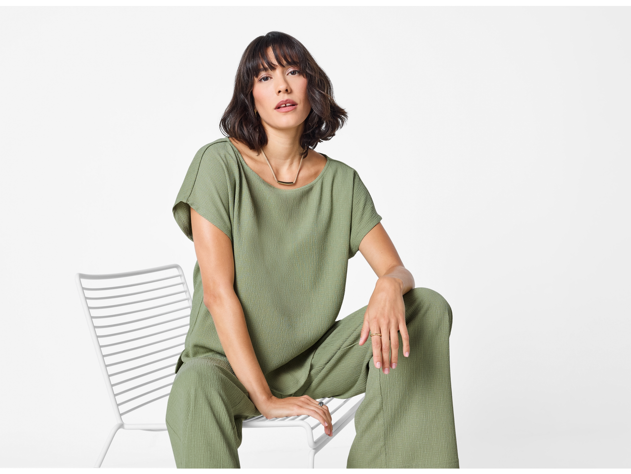 Žena u zelenim ESMARA kratkim hlačama i odgovarajućem topu, sjedi na bijeloj stolici.