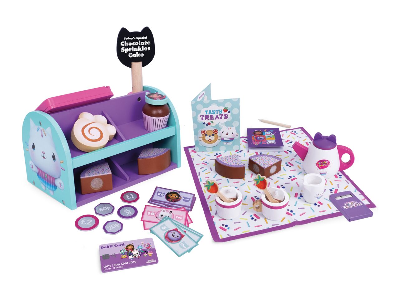 A play set with a cake stand, cakes, tea set, and play money, featuring a 'Chocolate Sprinkles Cake' sign.
