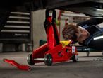 A red car jack lifting a vehicle, with a person working underneath.