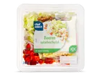 Een salade met sla, paprika, ui, kaasblokjes, walnoten en yoghurtdressing in een plastic verpakking.