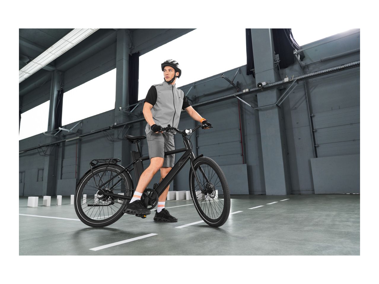 Man in cycling gear with a black e-bike in an industrial setting.