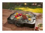 Electric grill with steak and vegetables on a wooden table outdoors.