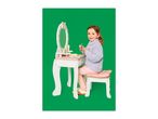 A young girl playing with a wooden dressing table and stool, holding a small stick.