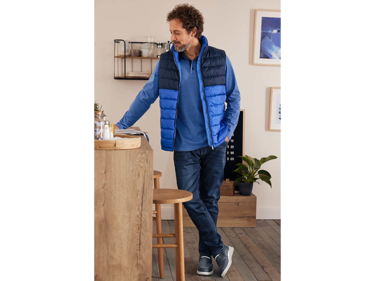 Άνδρας με μπλε μπουφάν και τζιν στέκεται δίπλα σε πάγκο κουζίνας.
