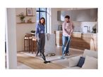 A woman vacuums a wooden floor while a man mops a tiled floor in a modern kitchen.