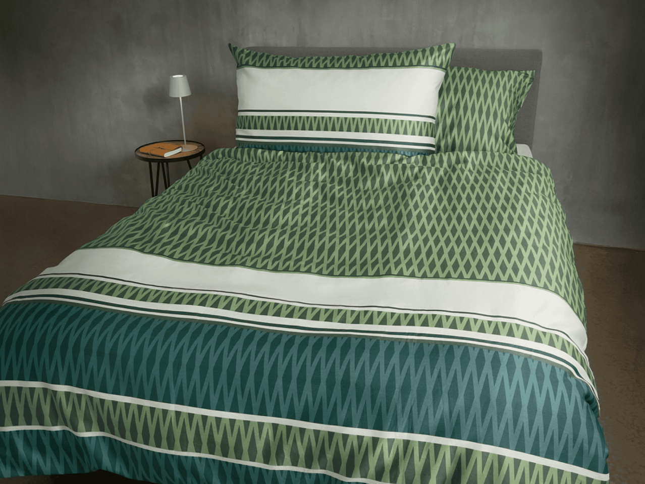 Bettwäsche-Set mit geometrischem Muster in Grün- und Weißtönen auf einem Bett.