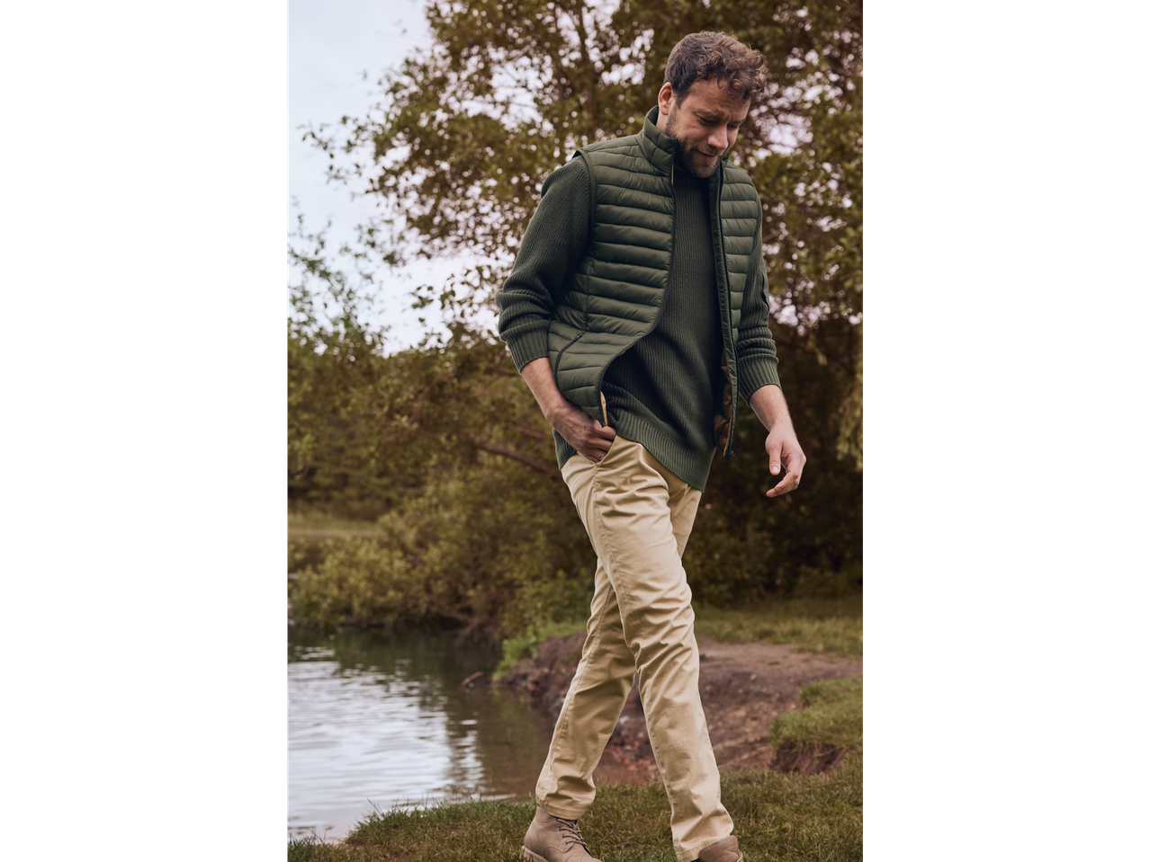 Homem com colete acolchoado verde Livergy e calças bege junto a um lago.