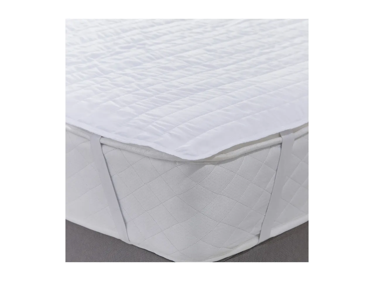 White quilted mattress protector with elastic straps on a bed.