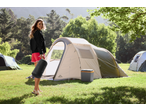 Mulher sorridente com saco de dormir CRIVIT em frente a uma tenda de campismo.
