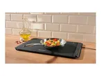 A black electric warming tray with a pan of cooked shrimp and vegetables, olive oil, and garlic.