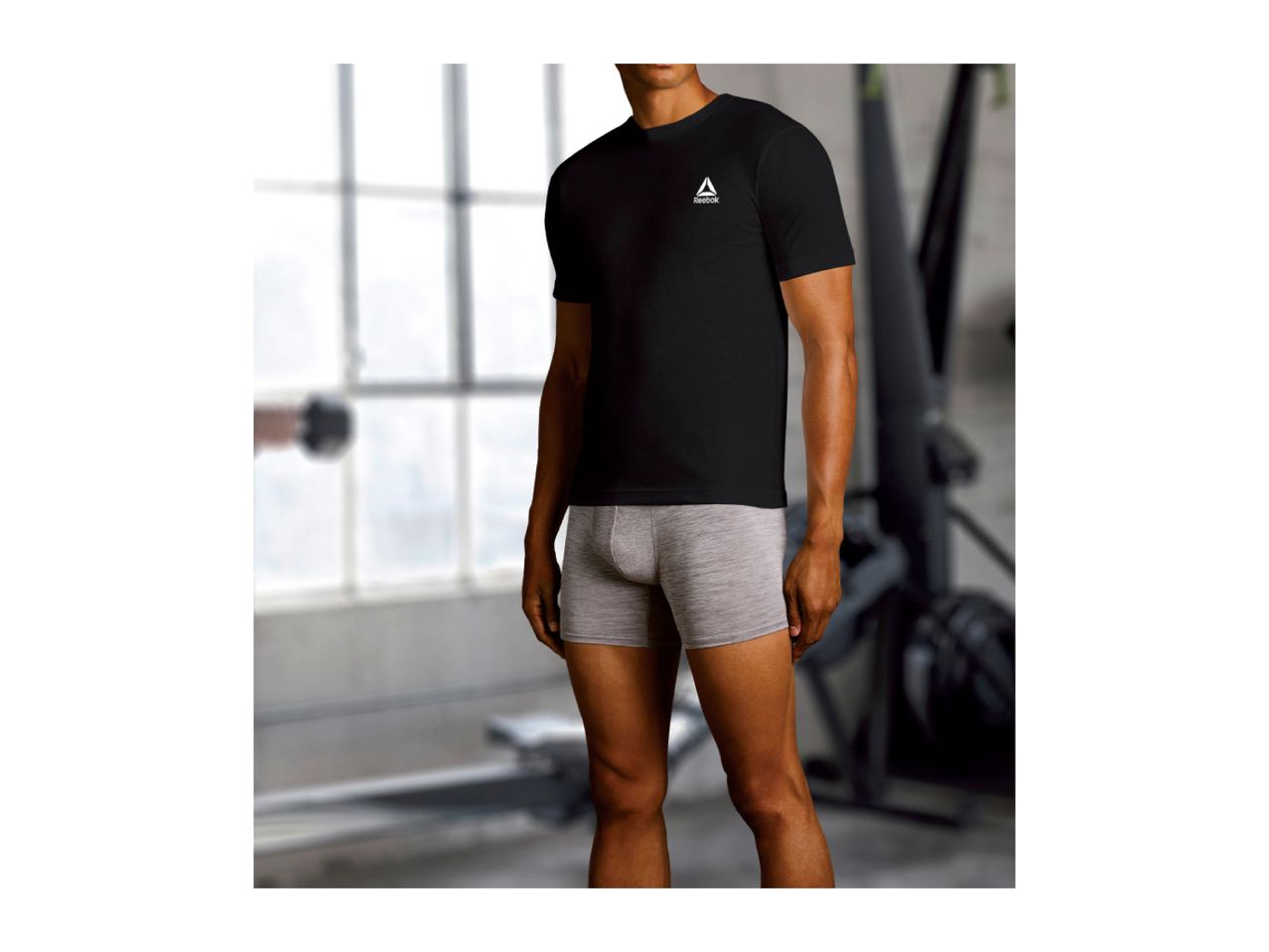Man in a black t-shirt and grey boxer briefs in a gym setting.