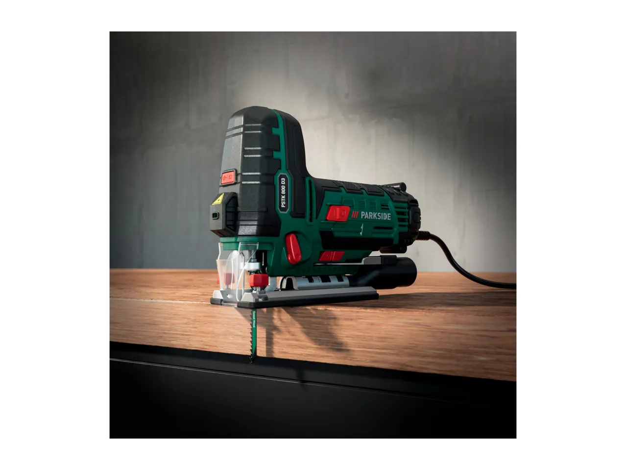 A green and black Parkside jigsaw on a wooden surface, with a blade extended downwards.