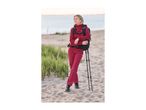 Woman in a red hiking outfit with a backpack and trekking poles on a sandy beach.