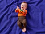 Baby in a pumpkin-themed outfit on a purple waffle-knit blanket.
