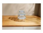 Three clear glass food storage containers with blue-rimmed lids stacked on a wooden counter.