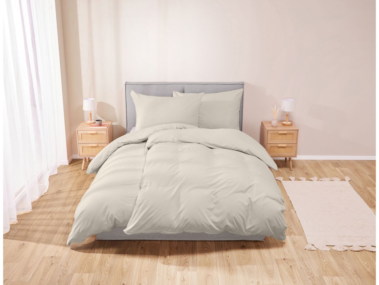 A bedroom with a bed featuring light beige bedding, two wooden nightstands, and a white rug.