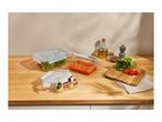 Glass food storage containers with fresh produce and sauce on a wooden counter.
