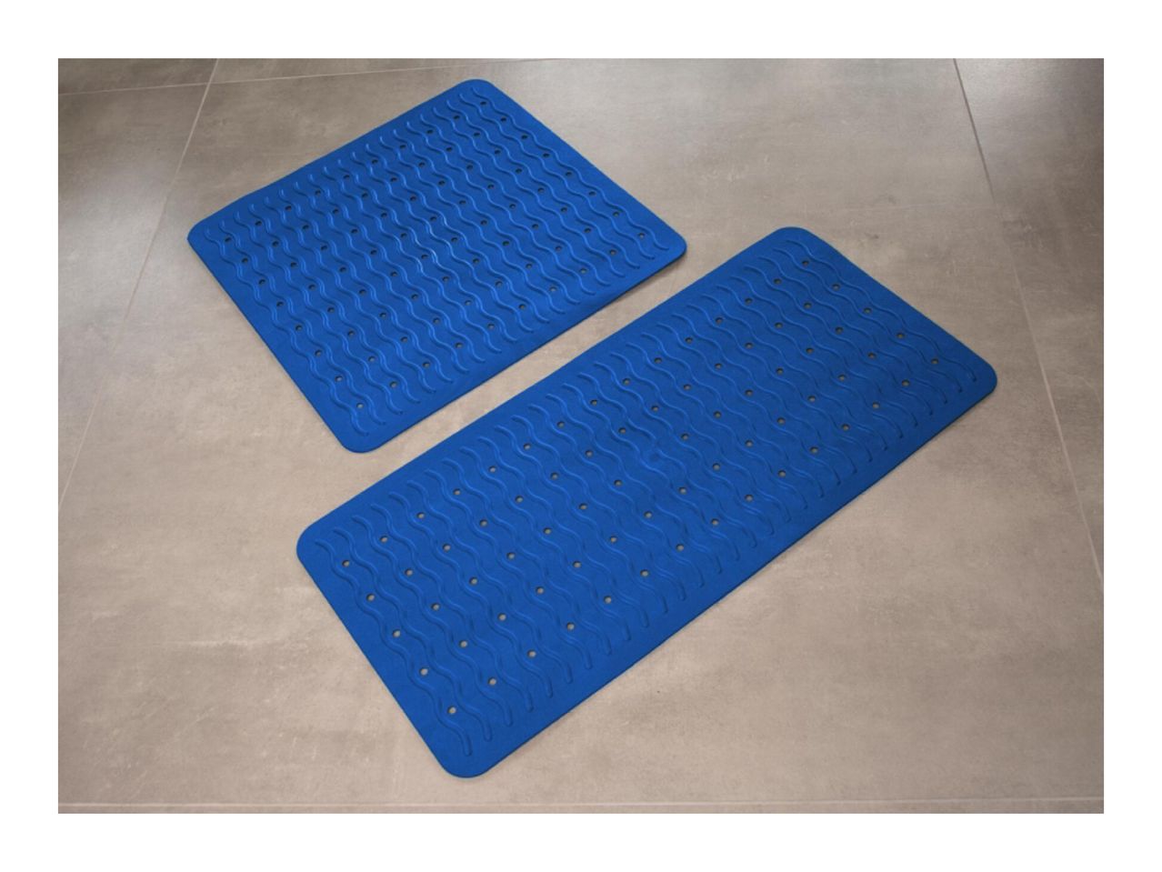 Two blue bath mats with a wavy pattern and drainage holes on a tiled floor.