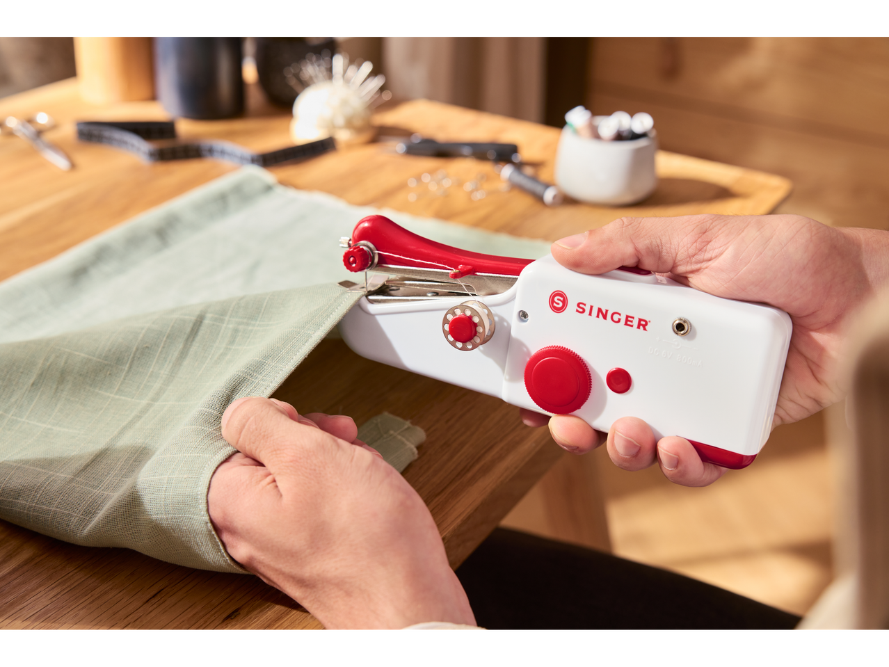 Person using a white and red Singer handheld sewing machine on light green fabric.