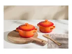 Two orange ceramic mini casserole dishes on a wooden board with a wooden spoon.