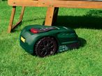 Robotic lawnmower on green grass under a wooden bench.